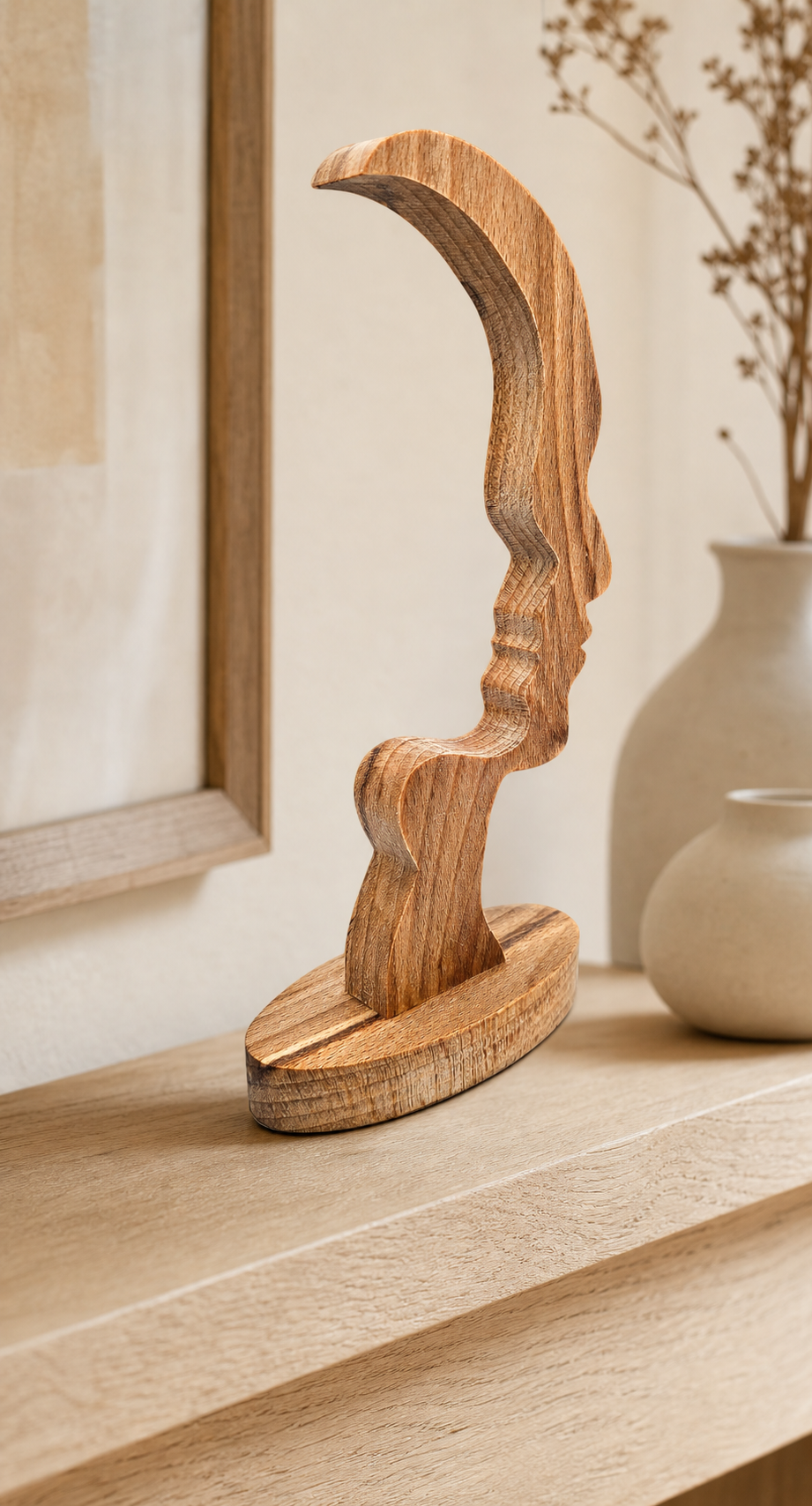 A sculptural wooden tabletop decor piece with a stylized curved human profile, displayed on a light wood mantel in a warm, neutral-toned interior setting.