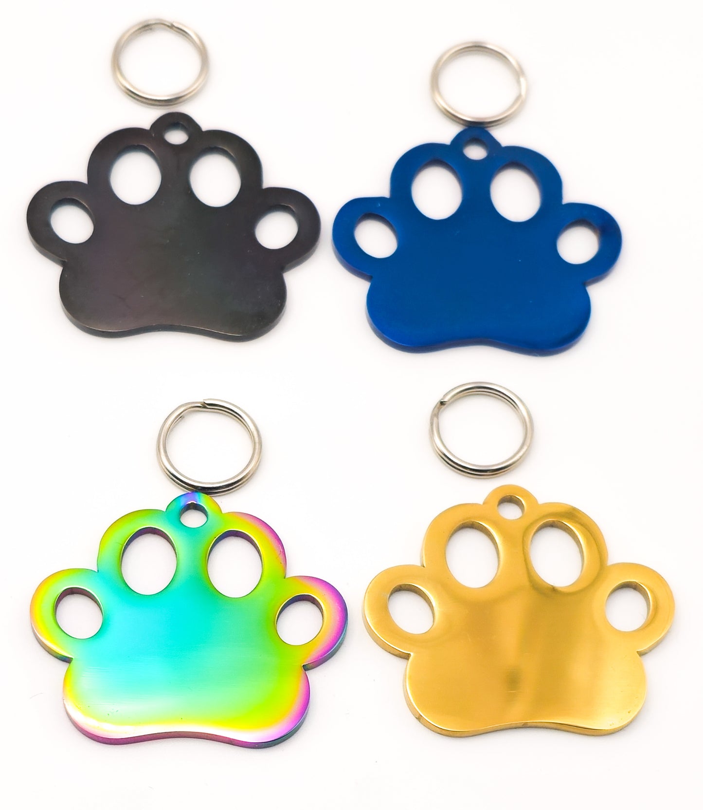 Four paw-shaped metal keychains or tags arranged in a 2x2 grid on a white background, showing different finishes: black, blue, iridescent rainbow, and gold, each with a silver key ring.