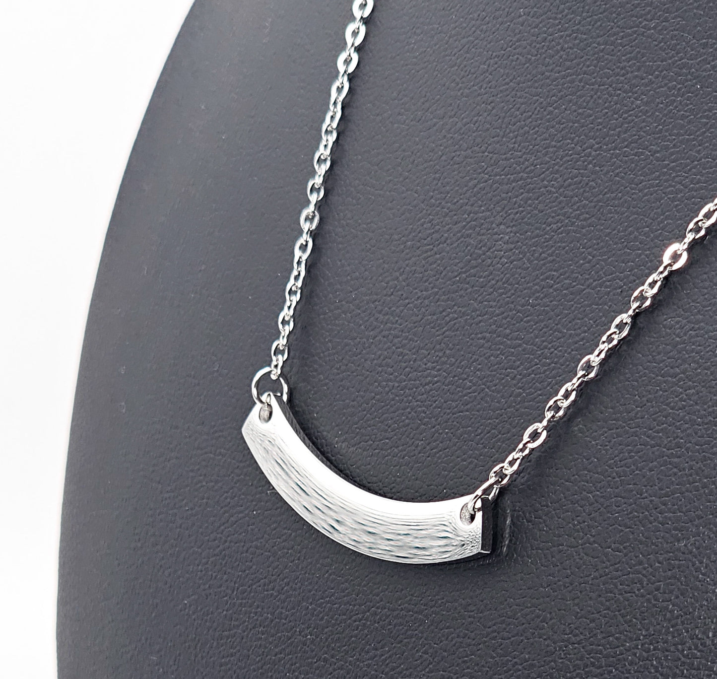 A silver crescent-shaped pendant necklace on a delicate link chain, displayed on a black textured jewellery bust.