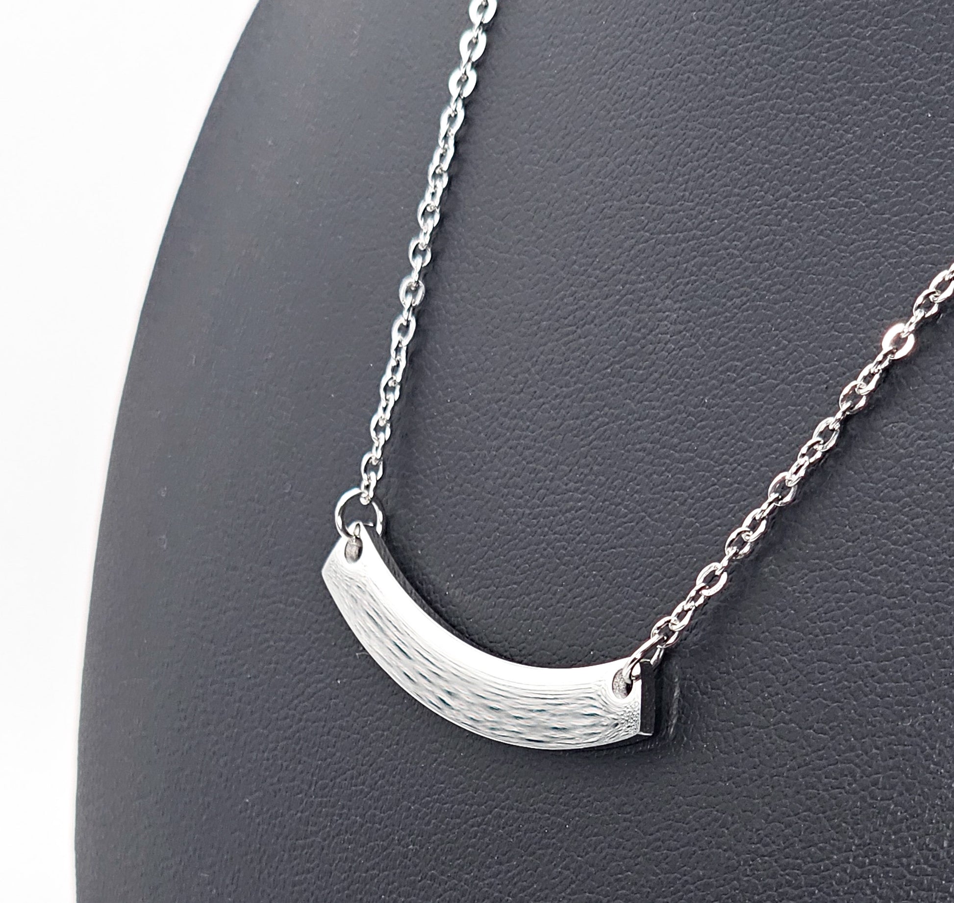 A silver crescent-shaped pendant necklace on a delicate link chain, displayed on a black textured jewellery bust.