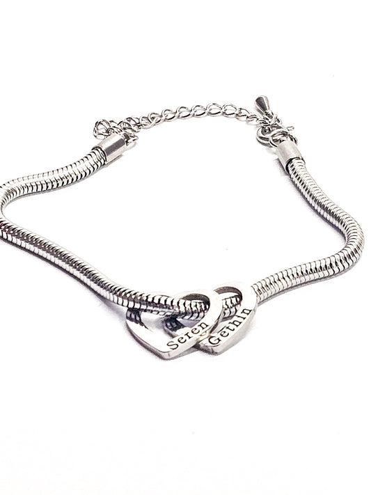 A silver-toned snake chain bracelet featuring two interlocking heart charms, one engraved with personalised engraving 