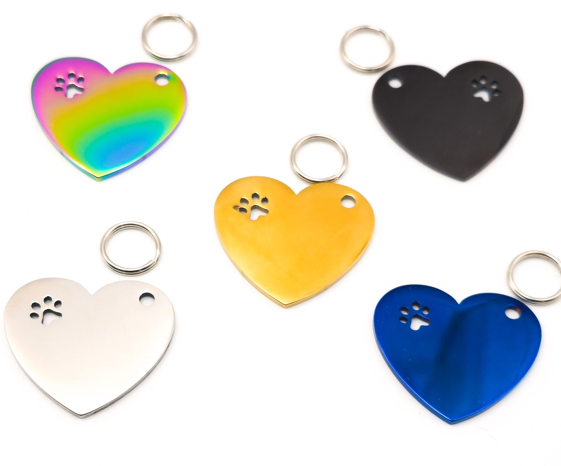 Five heart-shaped metal keychains in different colors (iridescent rainbow, black, yellow, silver, and blue) arranged on a plain white background. Each heart has a small paw print cutout near the top left and a split keyring at the top right.