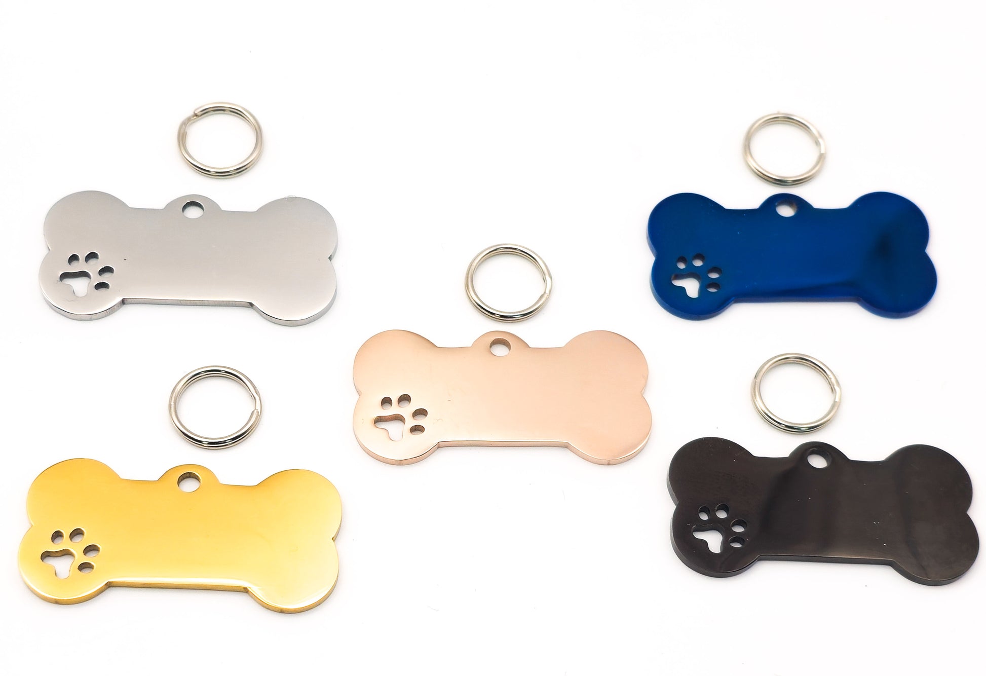 Five bone-shaped pet ID tags in silver, rose gold, yellow, blue, and black, each with a paw print cutout and a metal key ring, arranged on a white background.