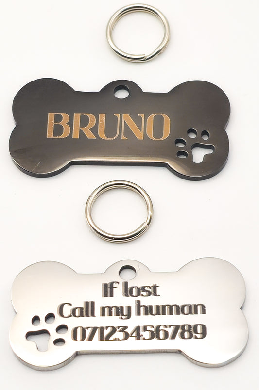 Two bone-shaped pet ID tags with key rings on a white background. The top tag is dark gray/black with gold lettering reading 'BRUNO' and a paw print.