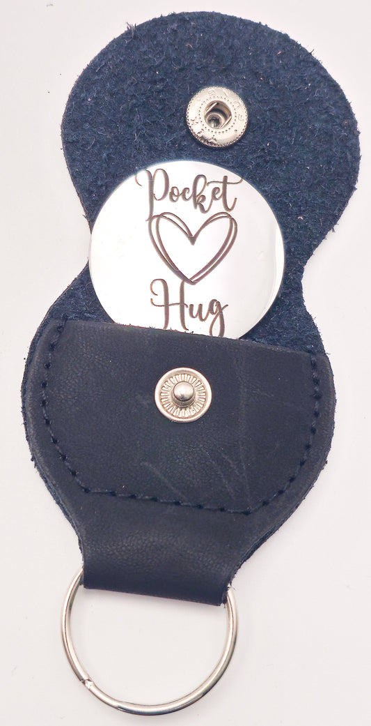 A dark navy blue faux leather keychain holder with a silver snap button and a metal key ring, featuring a white circular insert with the words 'Pocket Hug' and a heart graphic.